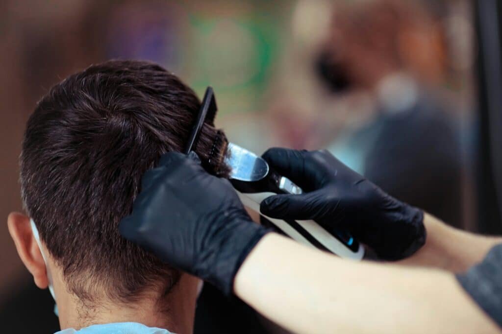 A hairdresser with security measures for Covid-19, holds a razor and a haircut for a man,